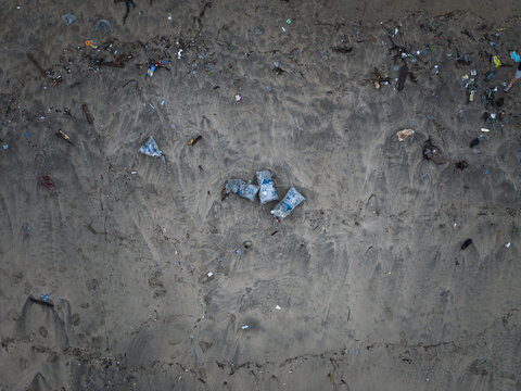 Aerial view of a polluted beach with scattered plastic waste contrasting against the dark sand, a somber reminder of environmental challenges, Badung, Bali, Indonesia.