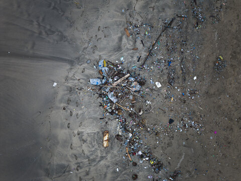 Aerial view of plastic waste scattered across the dark sands, marring the natural beauty of the beach, Badung, Bali, Indonesia.