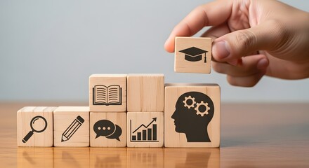 Hand placing graduation cap block on top of wooden blocks with education related icons on them