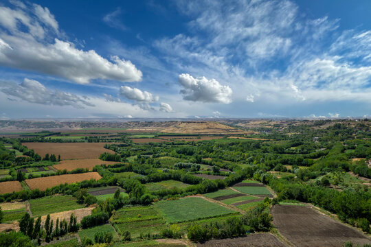 Panoramic view of Hevsel Gardens in Diyarbakir, Turkey, with lush green fields, golden crops and dramatic sky