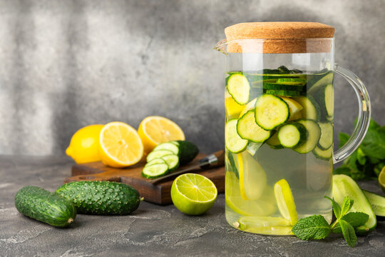 Cucumber water with lemon, lime and mint on a wooden table. Water infused with sliced ​​cucumber in a drinking glass. Tonic refreshing drink. Cucumber lemonade.Summer natural cooling drink.Copy space