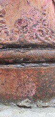 Close-up of an ornate antique cast iron column with rust and red peeling paint, featuring...