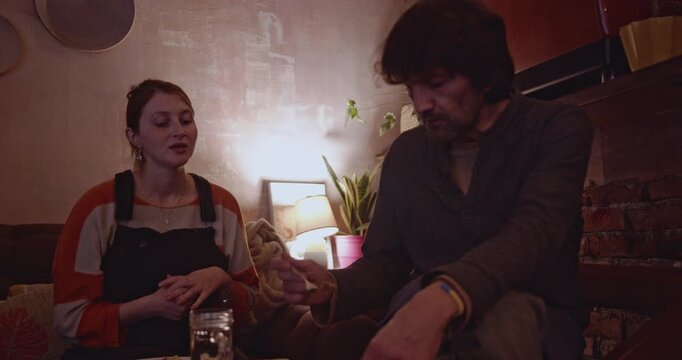 Friends enjoying a meal and conversation together in a cozy, dimly lit living room. They share stories, laughter, and create lasting memories.