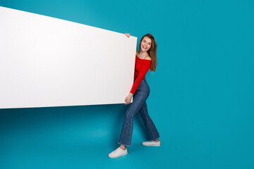 Charming young woman in a red top stylishly presents a large blank white sign against a vibrant...