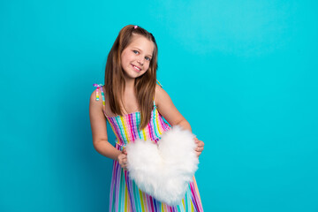 Cute girl in colorful striped dress holding a white fluffy heart prop against a turquoise background