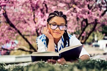 Young woman enjoying a relaxed day reading in a blooming park under the vibrant blossoms of springtime surroundings