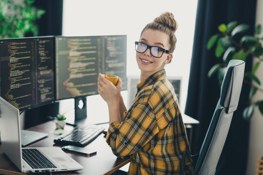 Young woman programmer working remotely in casual home office with multiple screens displaying code
