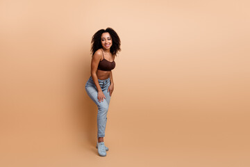 Trendy Casual Young Female with Curly Hair Wearing Stylish Outfit Posing Confidently on a Beige...