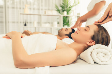 Caucasian couple enjoying relaxing anti-stress head massage and pampering facial beauty skin recreation leisure in dayspa modern light ambient at luxury resort or hotel spa salon. Quiescent