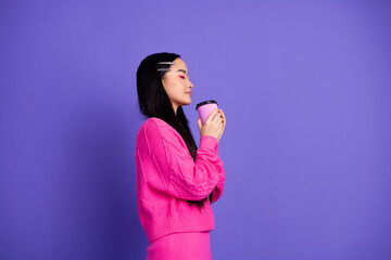Trendy young woman in pink sweater holding a vibrant coffee cup against a bold purple background,...