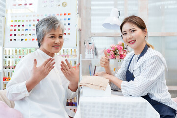 Senior Asian woman smiling proudly showing manicured hands after spa treatment sitting beside young...