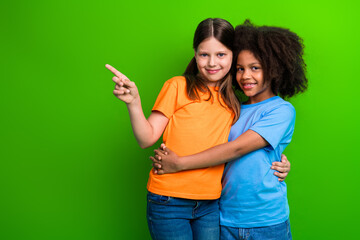 Two smiling girls hugging with a green background, one pointing at something, representing...