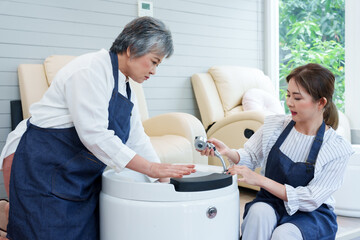 Senior Asian mother and young daughter testing spa equipment together inside new nail spa boutique...