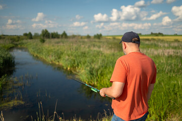 Man fishing by river in green countryside