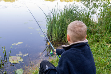 Boy sitting with fishing rod by river on sunny countryside day