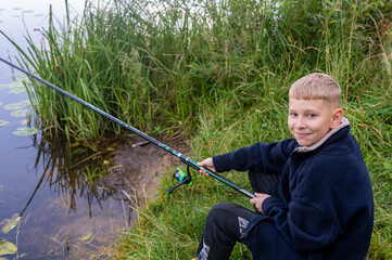 Boy sitting with fishing rod by river on sunny countryside day