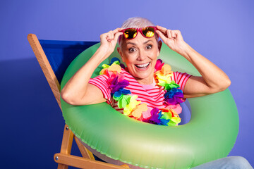 Cheerful elderly woman enjoying a summer vibe, wearing a colorful lei and sitting with a fun...