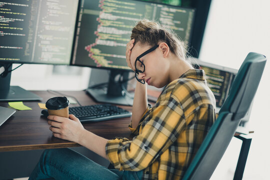 Concentrated female programmer working with code at the office, holding a coffee cup, appearing thoughtful and focused