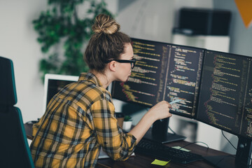 Young female programmer focusing on code development on multiple computer screens in a stylish...
