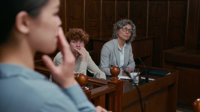Over the shoulder shot of nervous witness testifying in front of defendant and his lawyer in court