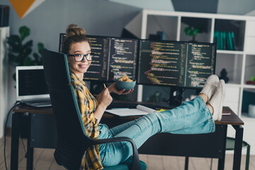 Confident female programmer multitasking with coding and snacks in a modern workspace at home office