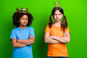 Two schoolgirls wearing playful crowns pose confidently with crossed arms against a bright green...