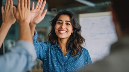 Gorgeous Indian woman in blue shirt high fiving coworkers at white board for concept about business development, no logos, no brands