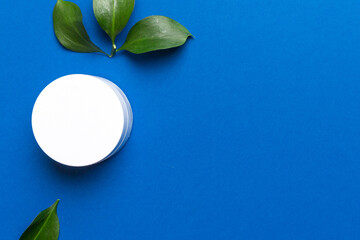 Organic cosmetic product with green leaves on color background. Copy space, flat lay