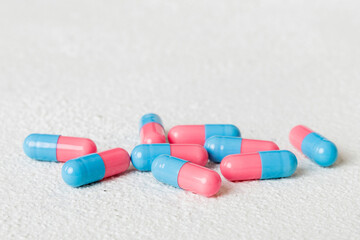 Heap of pink and blue pills on colored background. Tablets scattered on a table. Pile of red soft...