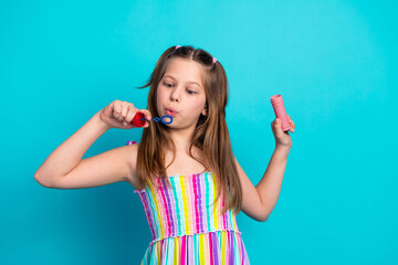 Charming schoolgirl in colorful dress blowing bubbles with a blue wand on a bright cyan background