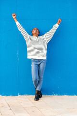 Joyful African woman celebrating with raised arms against blue wall