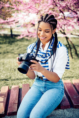 Cute woman with braided hair enjoying springtime in a park photographing blooming trees while...
