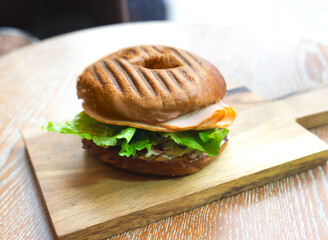 Grilled Pumpernickel Bagel Sandwich filled with Cranberry, Cream, Cheese, lean turkey slices and fresh green lettuce, served on a light wooden cutting board