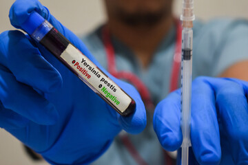 Text Yersinia Pestis of is written on a bottle sample with background of a doctor with a syringe in a medical glove mask. Medical concept
