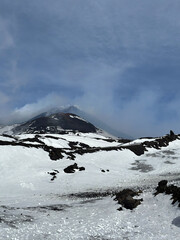 Majestic snow-covered mountain peak rises against a cloudy sky, showcasing rocky terrain and...