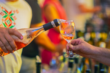 Male hand sommelier pouring wine into glass. Rose wine being poured into glass during festive event with warm lighting and blurred crowd. Concept of wine tasting, drink social gathering