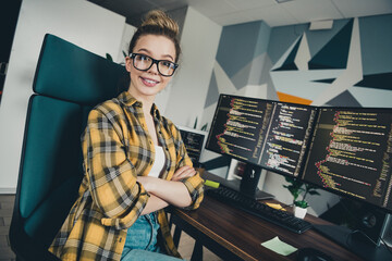 Young professional computer programmer smiling confidently while coding at a workspace with dual...