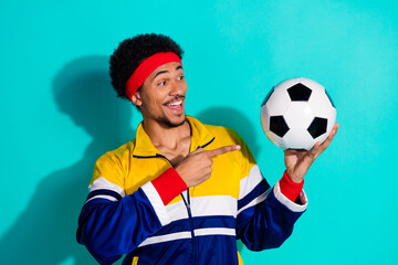 Young athletic man in retro sportswear holding a soccer ball, showing excitement against a vibrant...