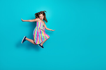Cheerful young girl in vibrant summer dress jumps with joy on a vibrant teal background...