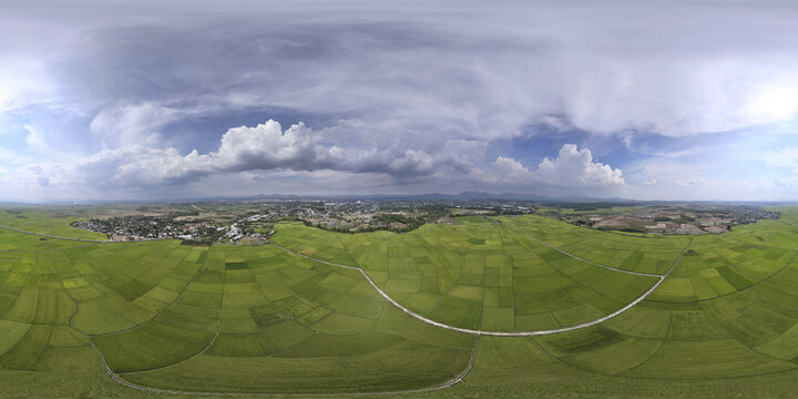 Aerial view of vibrant green rice paddies stretching towards a distant town beneath a vast sky filled with billowing white clouds, Kon Tum, Kon Tum, Vietnam.
