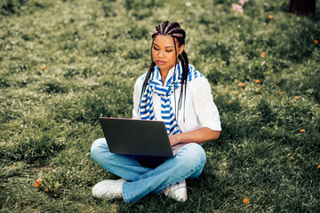 Young woman using laptop seated in park on sunny day embracing urban outdoor leisure and springtime...