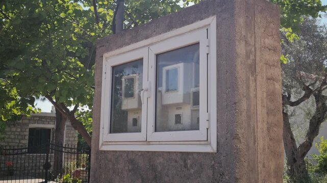 Outdoor electric meter box behind white framed glass on concrete wall, surrounded by greenery