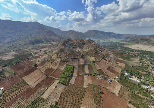Aerial view of fields sprawling across the landscape, contrasting with the rugged terrain and distant mountains, Chu Pah, Gia Lai, Vietnam.