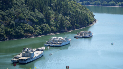 abandoned ships docked on a wide river with lush green forested banks