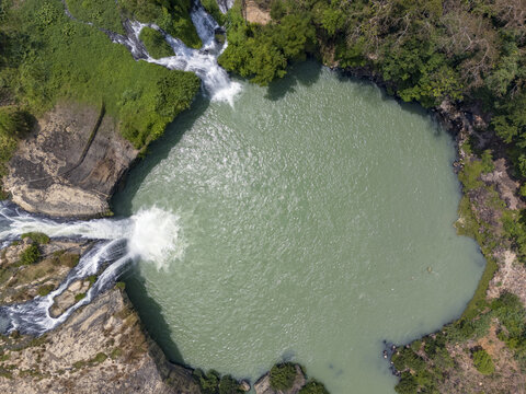 Aerial view of cascading waterfalls plunge into a serene, milky green pool, framed by rugged rocks and verdant foliage, Buon Ma Thuot, Dak Lak, Vietnam.