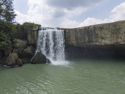 Aerial view of the Dray Nur Waterfall cascading powerfully into a jade-green pool, framed by rugged cliffs and verdant trees, Buon Ma Thuot, Dak Lak, Vietnam.