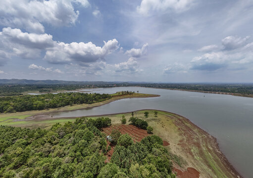 Aerial view of a tranquil lake embracing the land, contrasting the deep blues with the earthy reds and greens, Buon Ma Thuot, Dak Lak, Vietnam.
