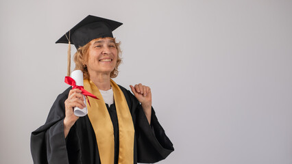 Happy senior woman in graduation gown holding diploma on white background. 