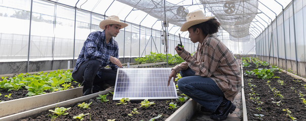 Farmer man inspecting a solar panel device for greenhouse for cultivation of vegetable food. Woman...