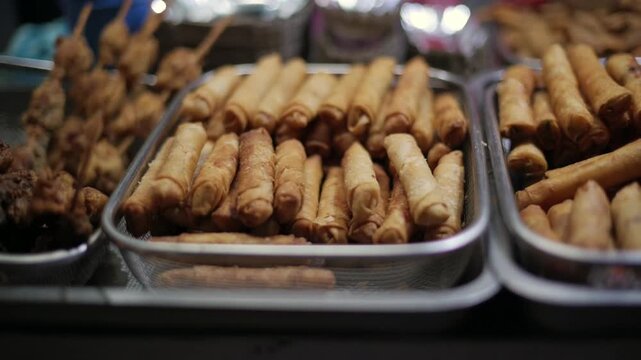 Golden fried spring rolls displayed in wire basket at traditional night food market in El Nido, Philippines. Spring rolls in basket at night market food stall in El Nido, Philippines
